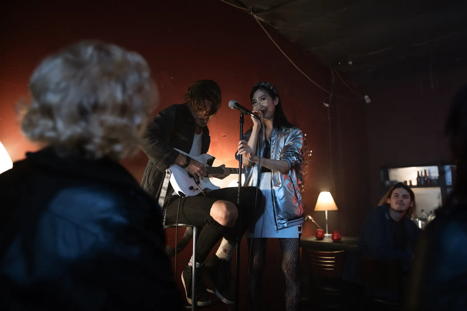 A guitarist and singer playing a set in a dim pub, a regular watching from the side