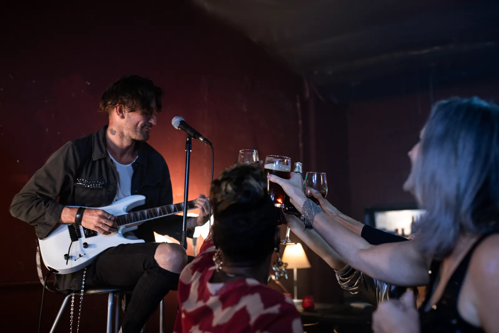 Regulars raising their glasses to a guitarist playing in a low-lit pub